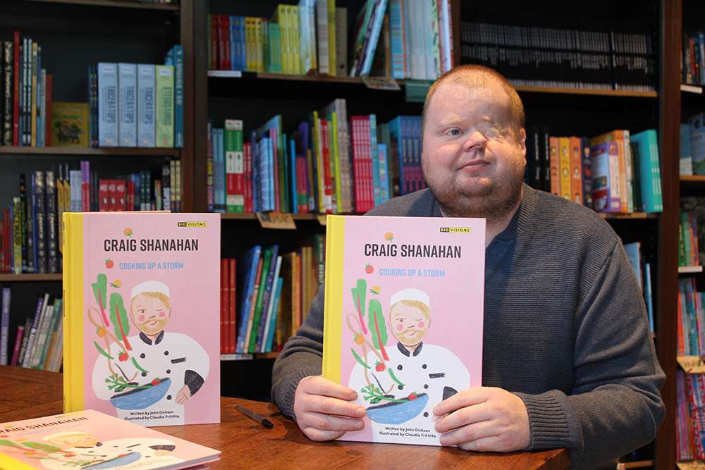 Craig Shanahan holding his children's book Cooking Up a Storm at a book signing event